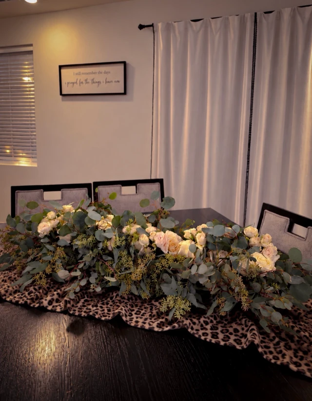 A long wedding table arrangement of white roses, baby’s breath and greenery