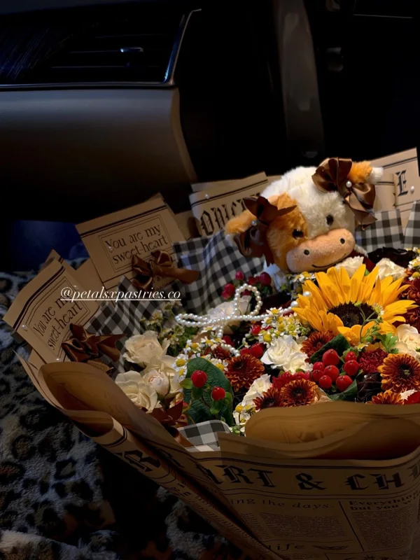 A bouquet with yellow sunflowers, white flowers, autumn colors and a small teddy bear