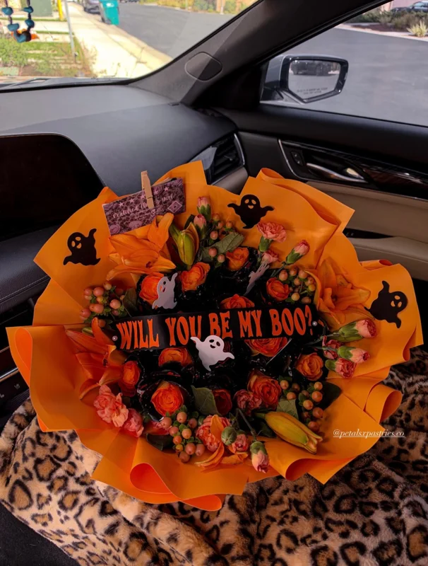 An orange and black Halloween bouquet with roses, a small ghost and a personalized message