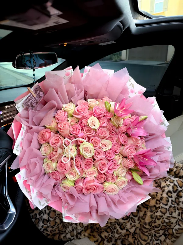 A large pink rose and lily bouquet with a tiara, white monogram and pink wrapping