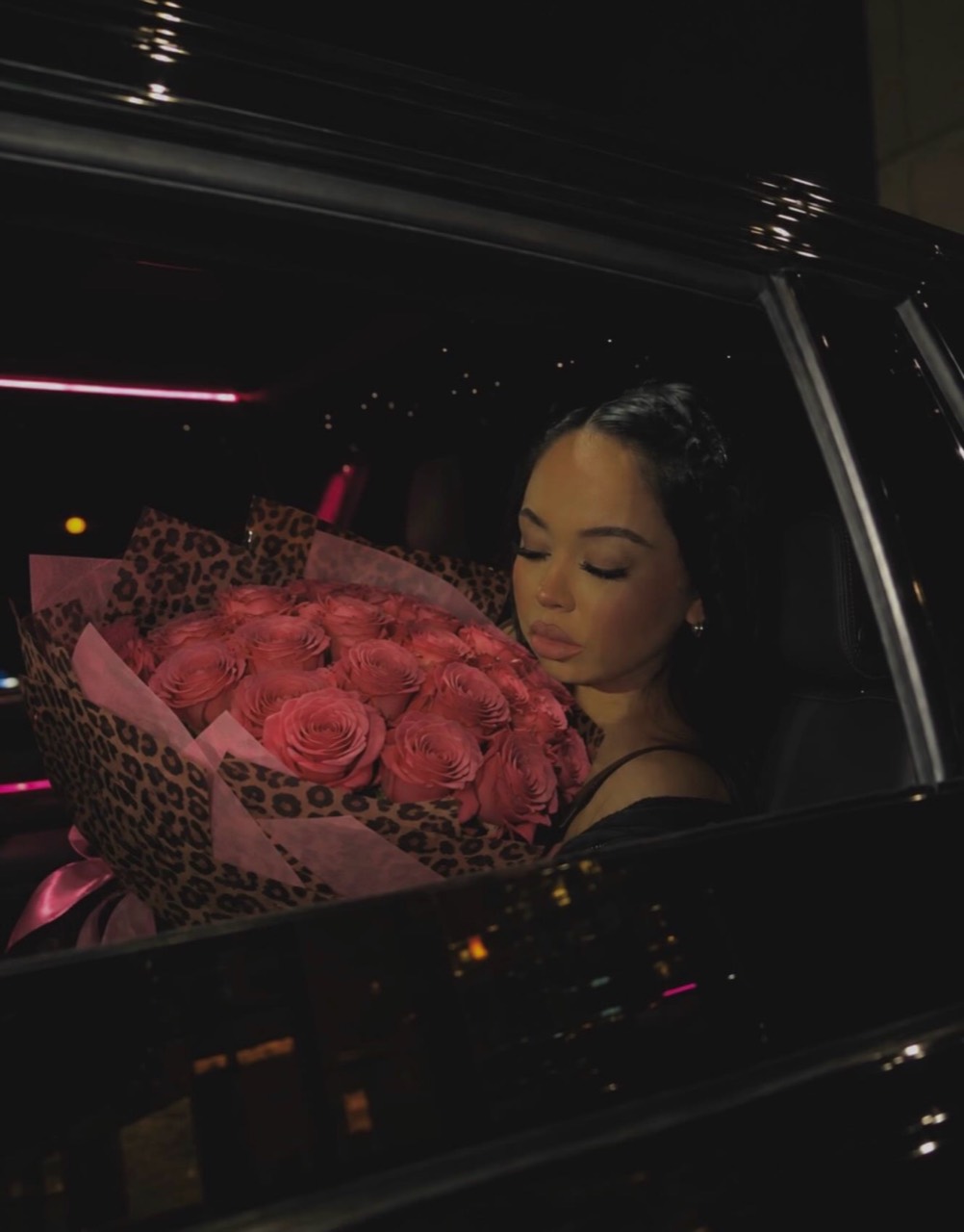 Kayla holding pink roses wrapped in animal-print paper beside a car window