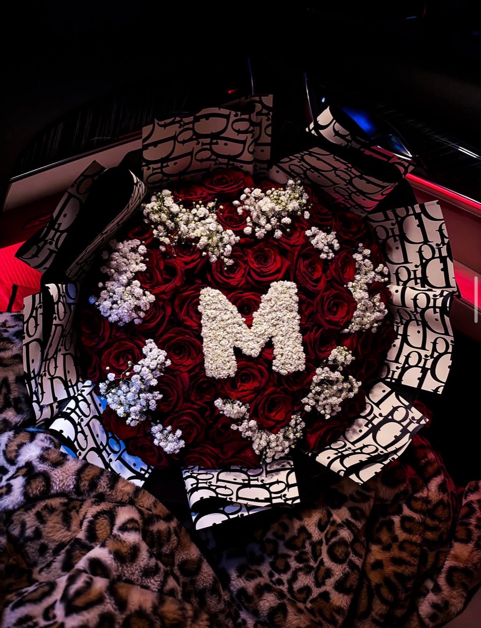 Red roses and baby’s breath with a white floral M, wrapped in pink and black paper