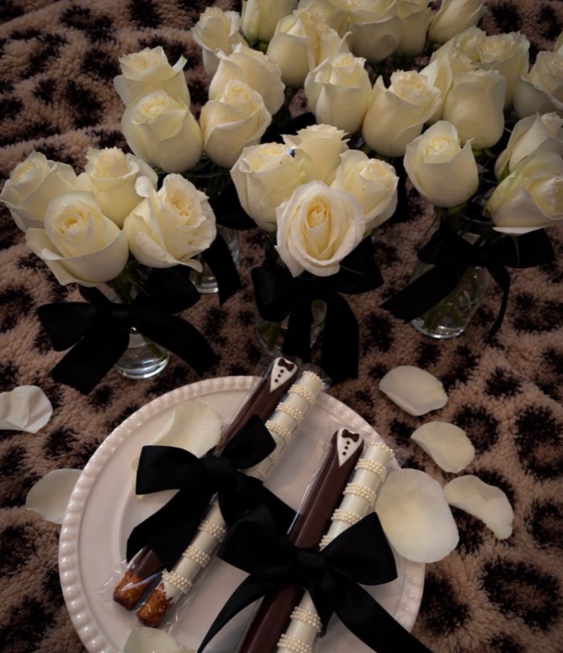 White roses in small vases with black bows and matching decorated wedding treats